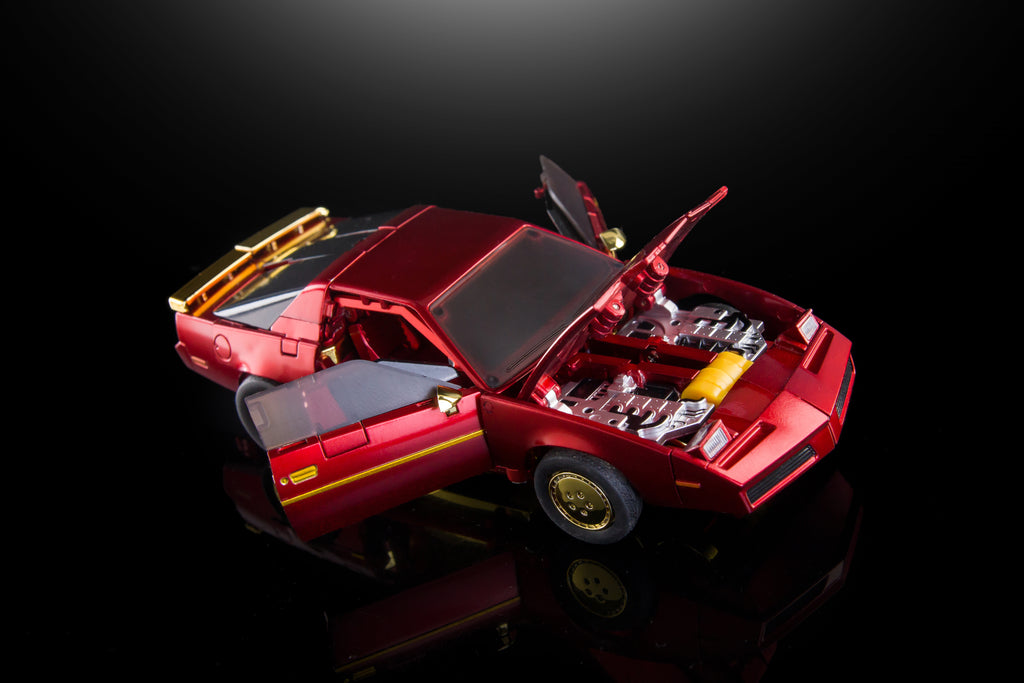 A metallic red model car with its doors and hood open, revealing a detailed engine bay, photographed on a glossy black reflective surface against a dark background.