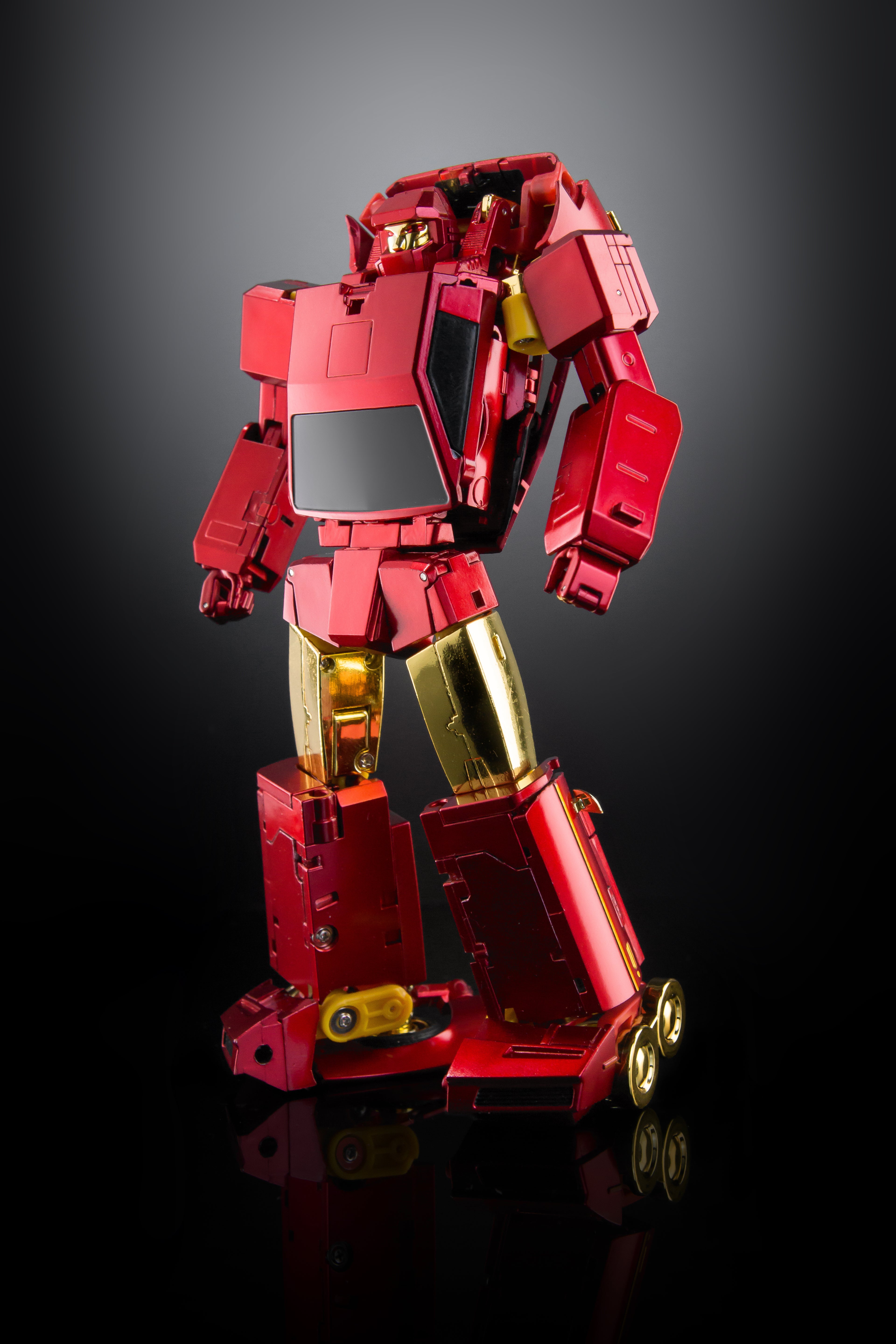 A metallic red and gold robot action figure or collectible model standing on a reflective black surface against a dark gray gradient background.