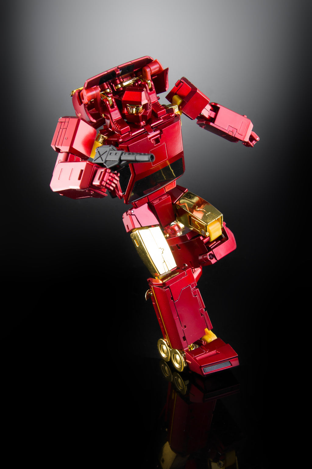 A metallic red and gold action figure or collectible robot toy posed dynamically against a dark gradient background with a reflective black surface below.