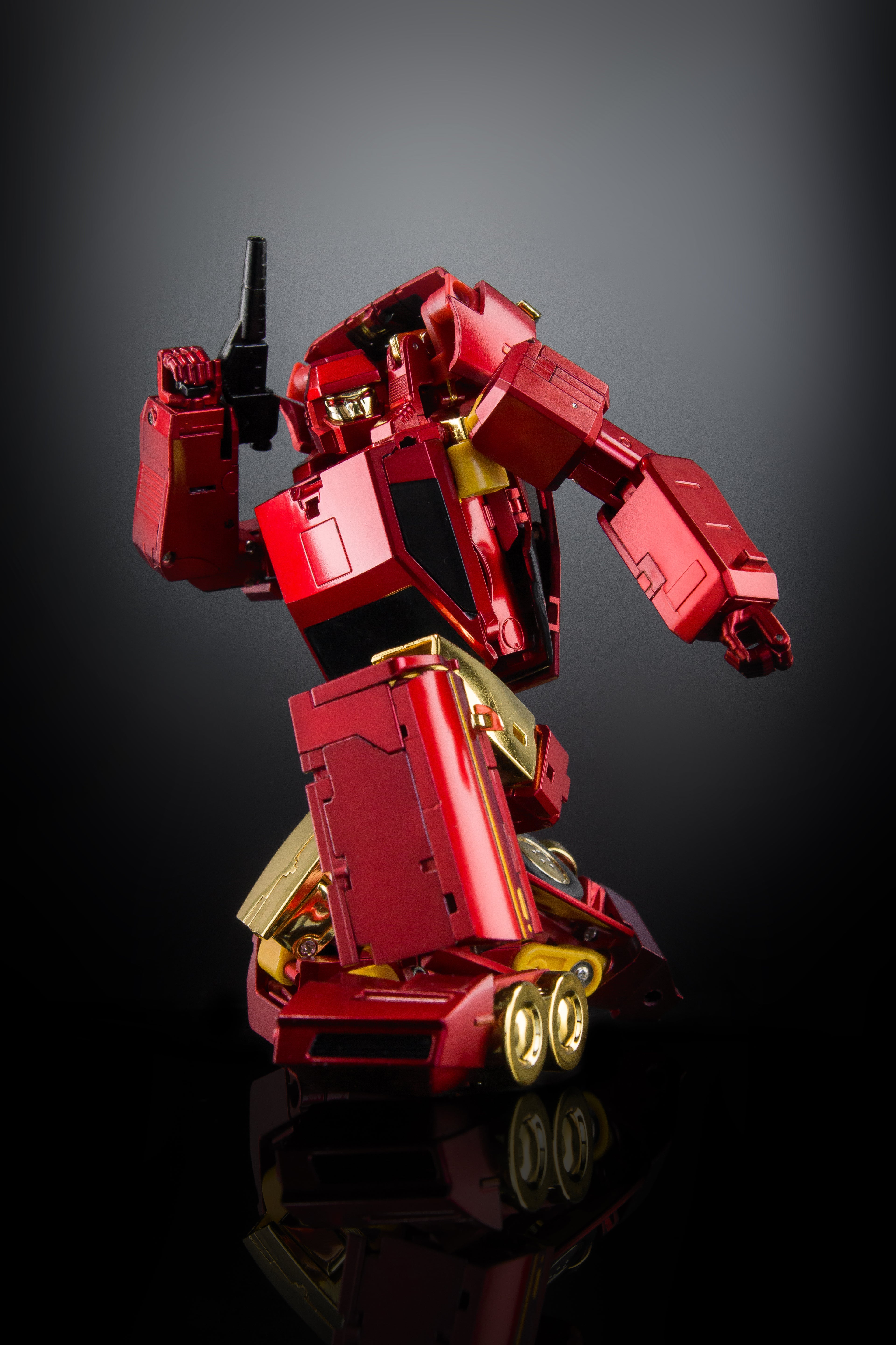 A red and gold metallic robot toy figure posed dynamically on a reflective black surface against a dark gray gradient background.